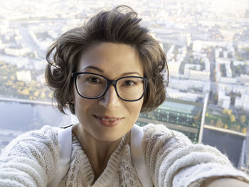 Pretty curly woman in eyeglasses takes selfie photo. selfportrait on cityscape background.