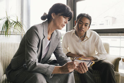 Businesswoman discussing over placard with non-binary person while sitting at office