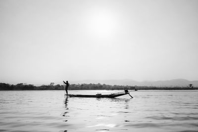 Silhouette man on boat in lake against sky