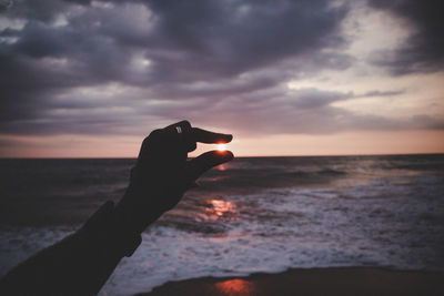 Hand against sea during sunset