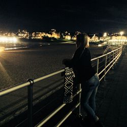 Rear view of woman standing in illuminated city at night