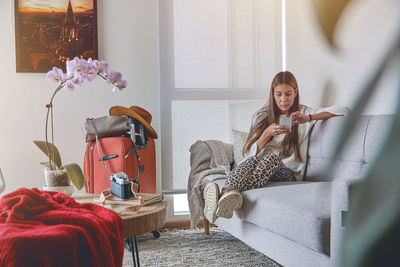 Attractive young women sitting on the room floor and looking forward to go on vacation.