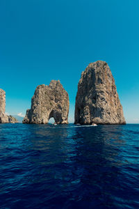 Rocks in sea against clear blue sky