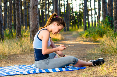 Side view of young woman using phone while sitting on land