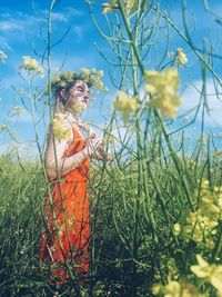 Woman in a red dress in a field of yellow flowers on a sunny day against a blue sky