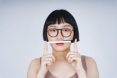 Portrait of young woman holding eyeglasses against white background