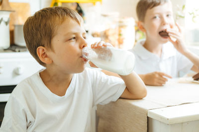 A boy is drinking milk from a bottle in the kitchen at home. morning breakfast with milk. 