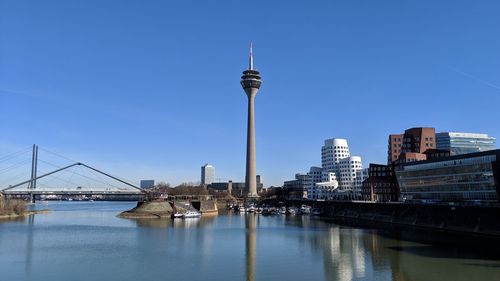 View of modern buildings by river against sky in city