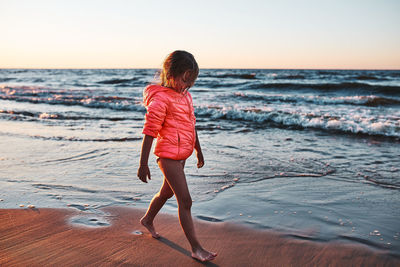 Little girl walking barefoot on a beach at sunset during summer vacation