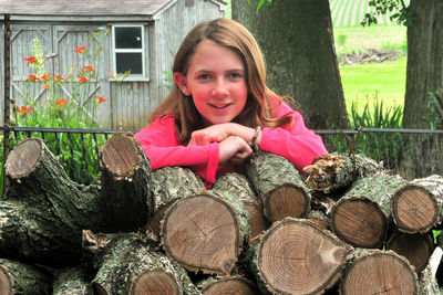 Portrait of teenage girl leaning stacked logs against house