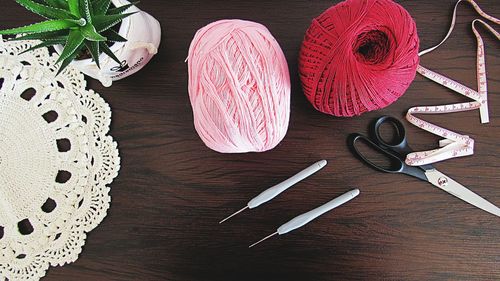 Directly above shot of wool ball with crochet and scissor over table