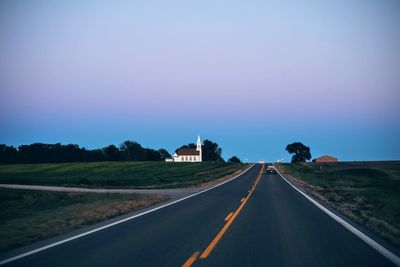 Car moving on road amidst field against clear sky