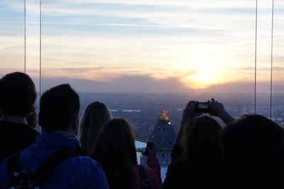 Rear view of people photographing cityscape against sky during sunset