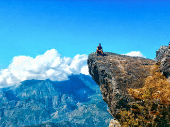 Man sitting on rock against blue sky