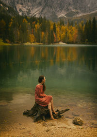 Woman in orange dress sitting on a log on the shore of a lake, italy