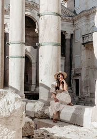 Young woman in beautiful dress sitting on wall of diocletian's palace in split, croatia.