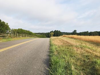 Empty road amidst field against sky