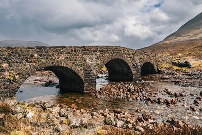 Arch bridge over river against cloudy sky