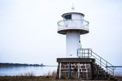 Lighthouse by sea against clear sky