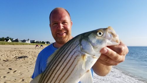 Man holding fish in sea against clear blue sky