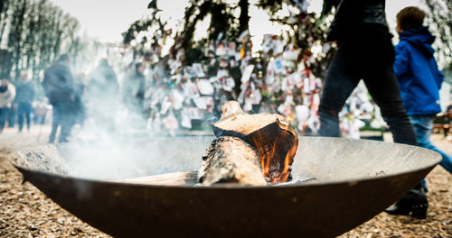 Close-up of fire pit on field with people background