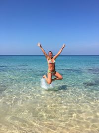 Portrait of smiling young woman in sea against clear blue sky