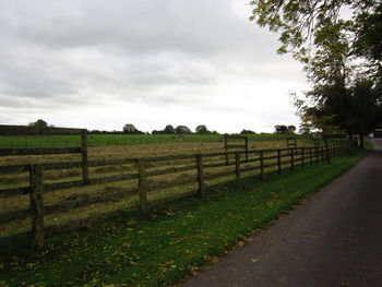 Empty road on grassy field against cloudy sky
