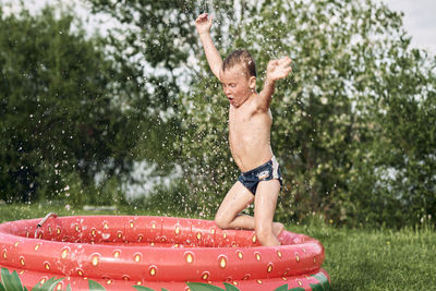 Boy jumps in the pool in the summer on the lawn, drops of spray in the sun.