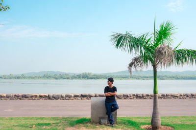 Full length of man sitting by sea against sky