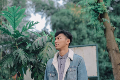 Young man looking away against trees