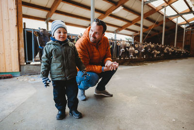 Father and son smiling in barn with cows behind during winter