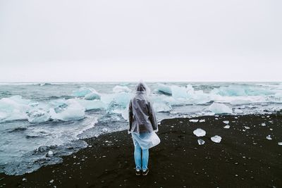 Rear view of woman standing on shore against clear sky