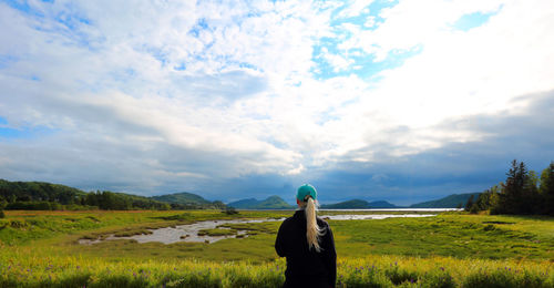 Rear view of woman standing on grassy field against cloudy sky