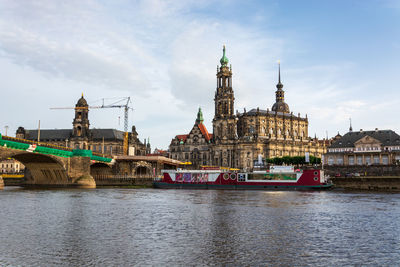 Boats in river by buildings against sky