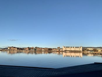 Buildings by river against clear blue sky