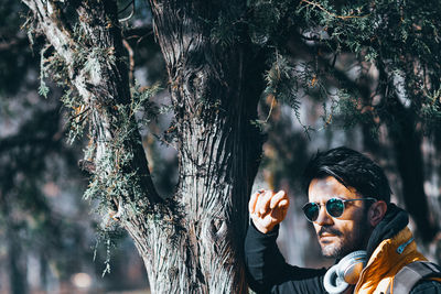 Portrait of young man by tree trunk in forest
