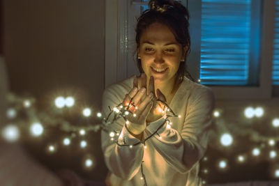 Woman smiling while holding illuminated string lights in darkroom