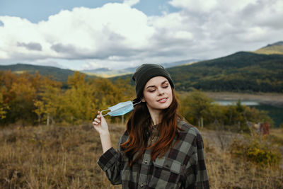 Portrait of smiling young woman standing on land against sky