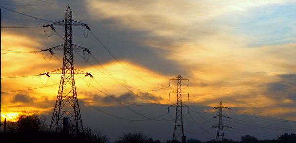 Low angle view of silhouette electricity pylon against dramatic sky