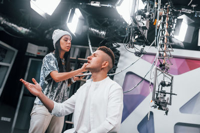 Young man is preparing for tv online broadcast. woman helps with make up.