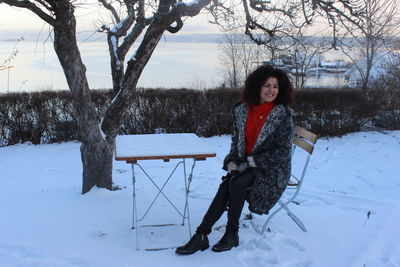 Portrait of woman sitting on bench at snow covered field