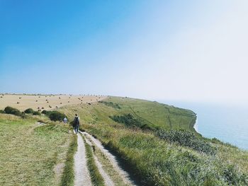 Man walking on landscape against clear blue sky