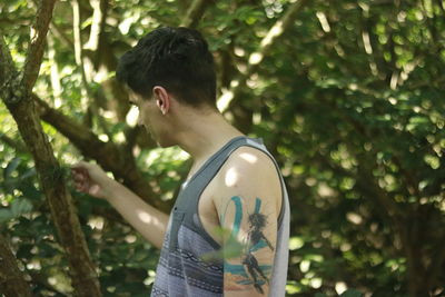 Man with tattoo on hand standing against trees during sunny day