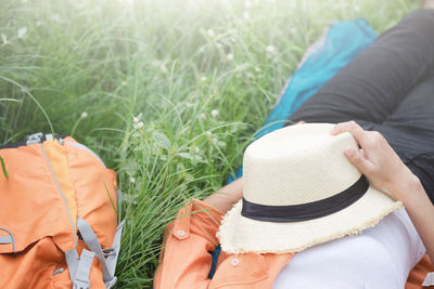 Midsection of woman holding hat while lying on grassy field