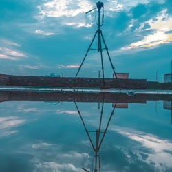 Electricity pylon by lake against sky during sunset