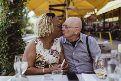 Senior couple kissing each other while sitting at sidewalk cafe