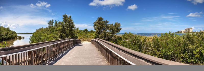 Footbridge amidst plants and trees against sky