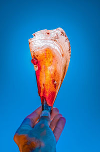 Close-up of hand holding ice cream against blue background