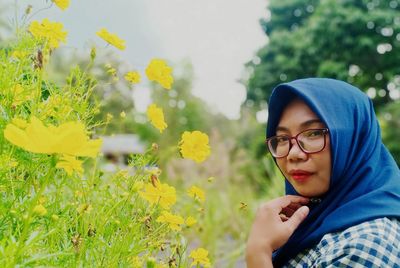 Portrait of woman in hijab standing by yellow flowering plant