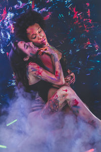Young women wearing bikini while covered in body paint at sitting at nightclub